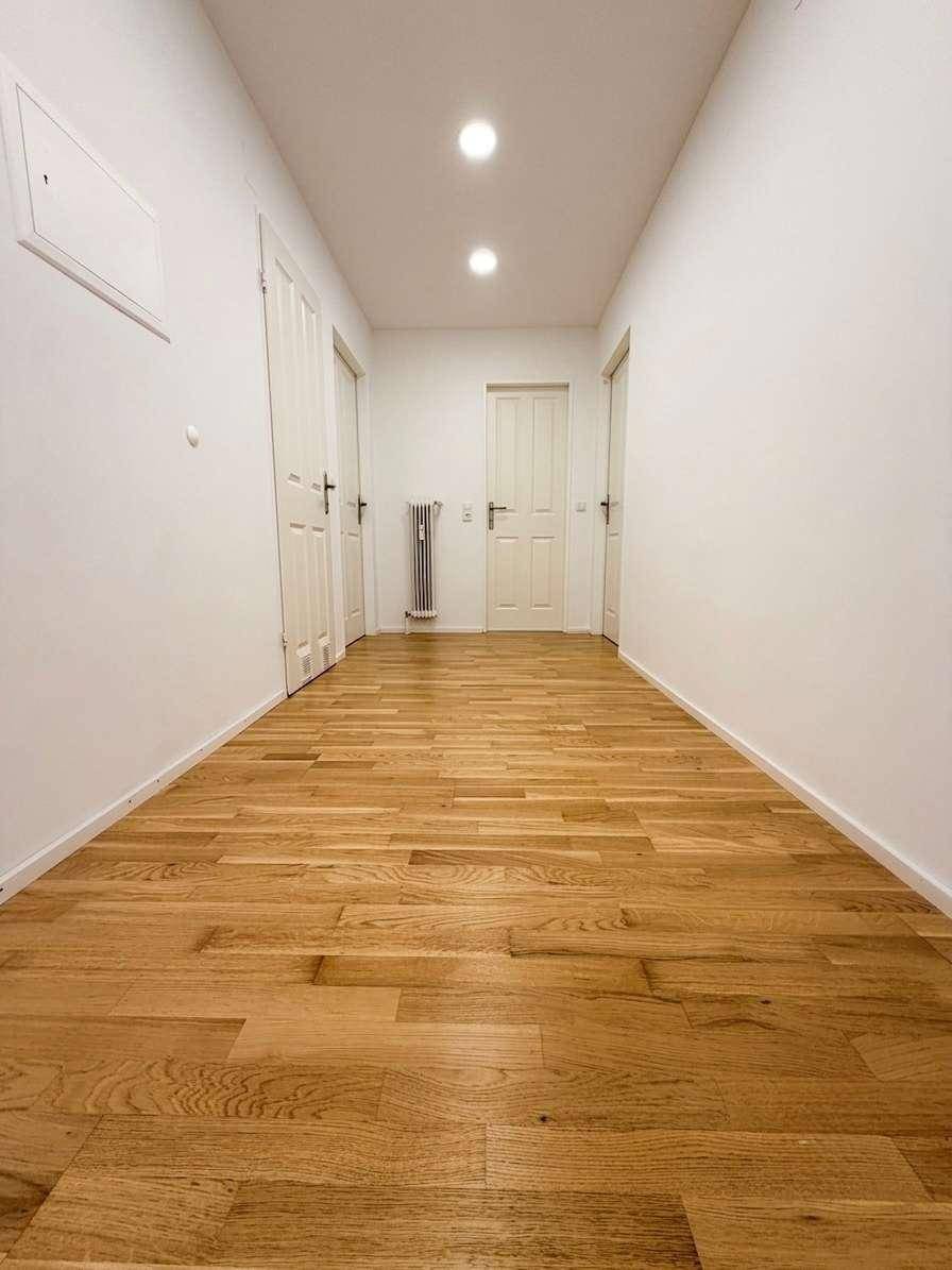 Langer, heller Flur mit Holzboden und mehreren Türen, ausgestattet mit einem Heizkörper.