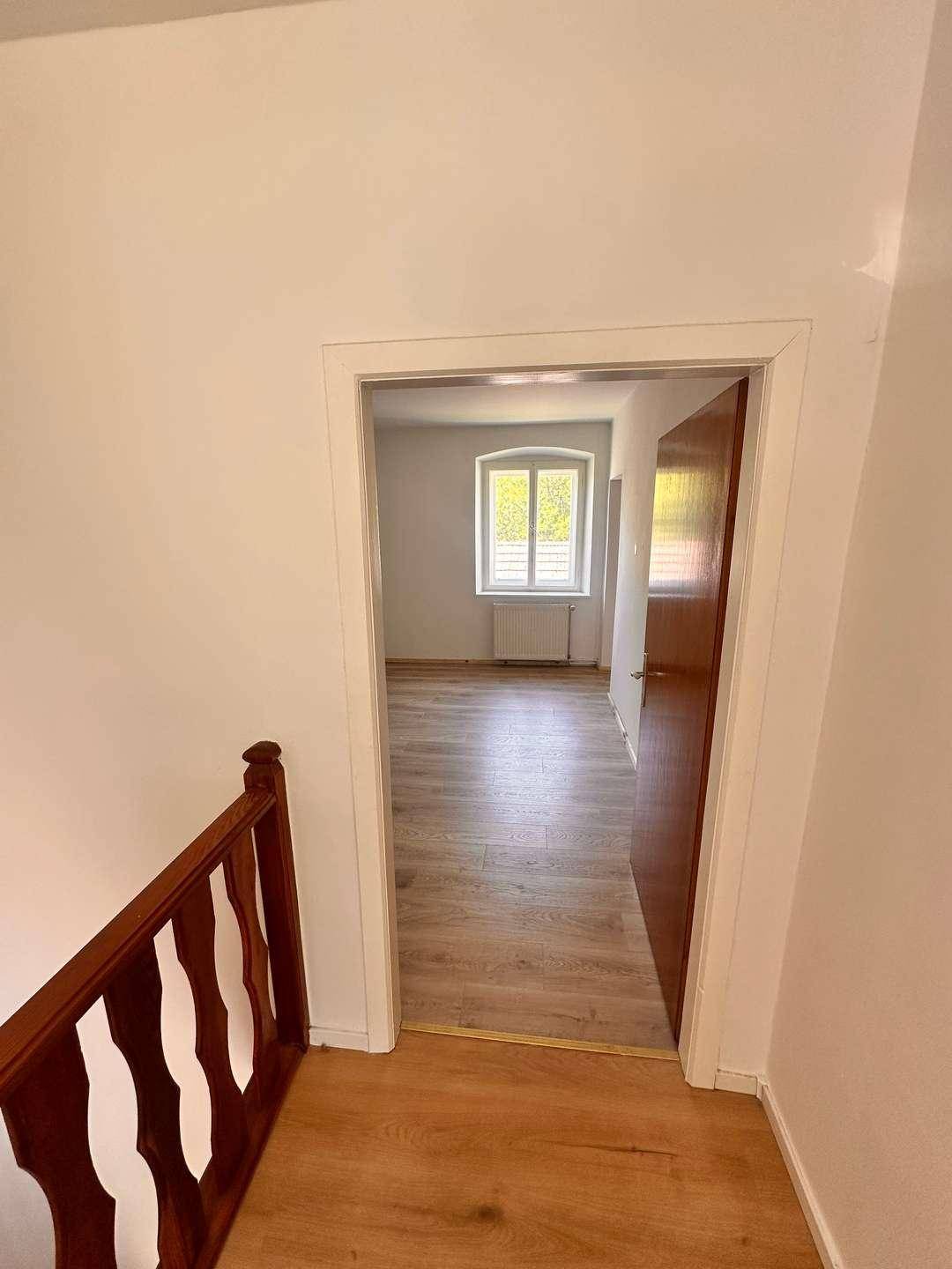 Blick vom Flur in ein helles Zimmer mit Holzoptikboden und einem Fenster.