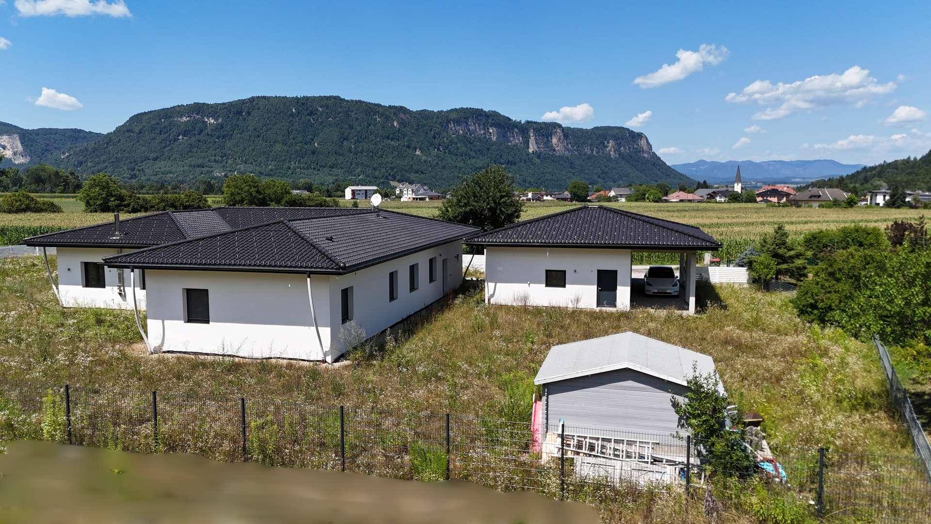Zwei moderne Häuser mit Carport und Schuppen, umgeben von Natur und Bergpanorama.