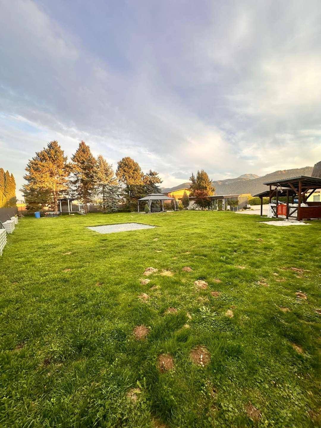 Weitläufiger grüner Garten mit Bäumen, einem Pavillon und Blick auf die Berge.