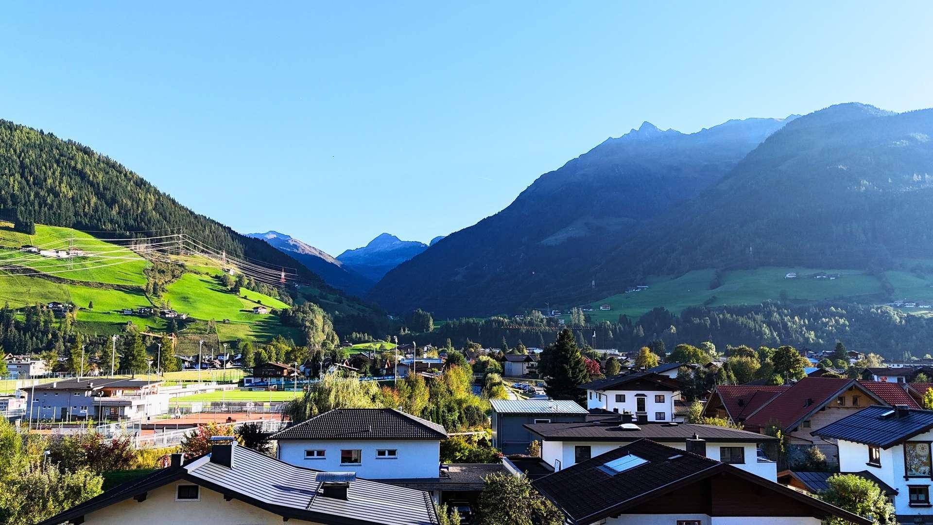 Panoramablick auf ein Tal mit Häusern und majestätischen Bergen im Hintergrund.
