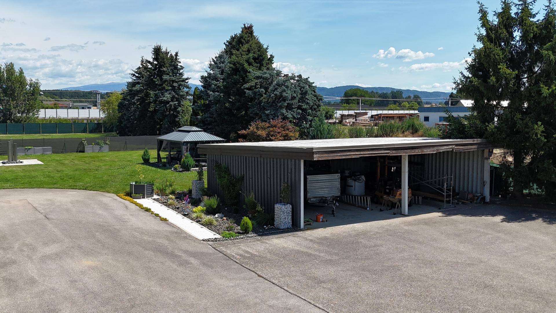 Gepflegter Gartenbereich mit Rasenfläche, Pavillon und einem Carport im Vordergrund des Anwesens.