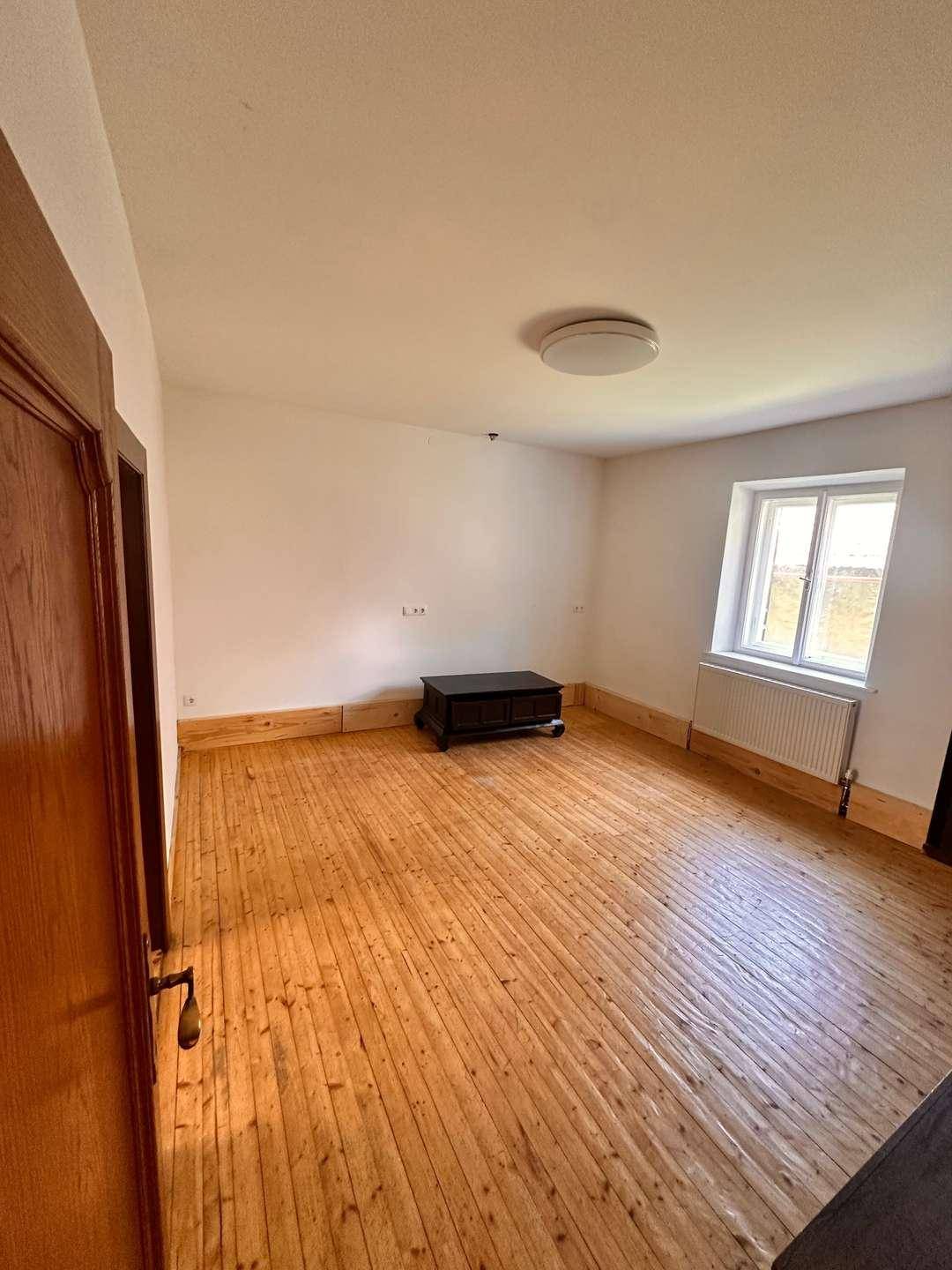 Geräumiger Raum mit Holzdielenboden und weiß gestrichenen Wänden, ideal für Wohnzwecke.