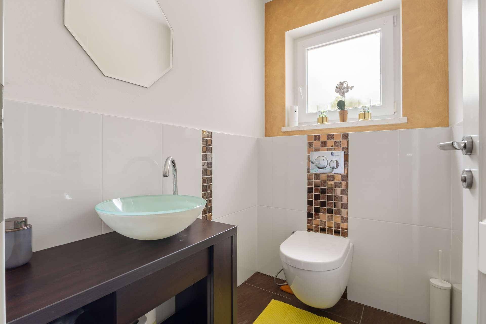 Gäste-WC mit modernem Waschbecken, Wand-WC und dekorativen Fliesen.