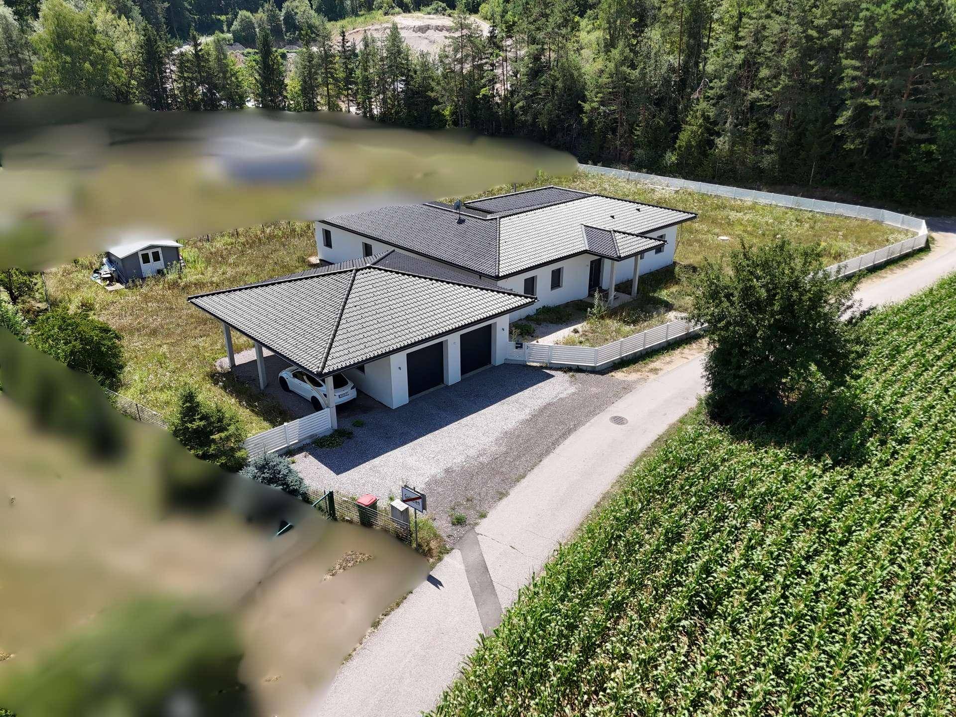 Luftaufnahme eines modernen Einfamilienhauses mit Carport und großem Grundstück in ländlicher Umgebung.