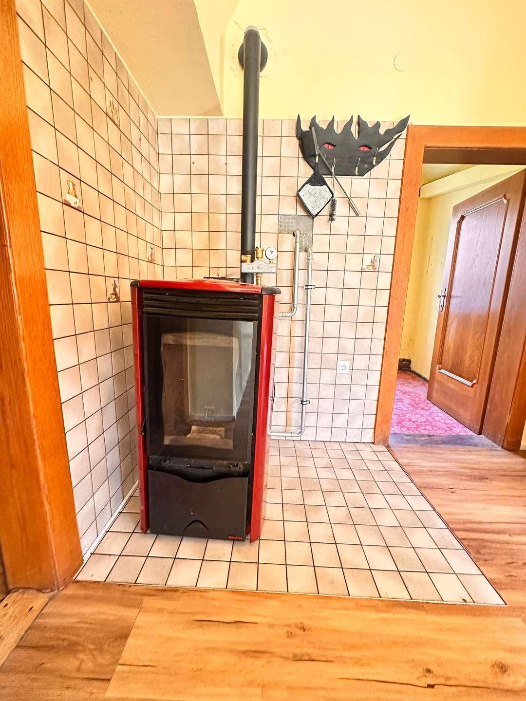 Detailansicht eines roten Holzofens mit Kaminrohr und gefliestem Hintergrund.