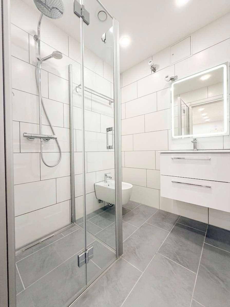 Modernes Badezimmer mit begehbarer Dusche, Bidet und weiß-grauen Fliesen.