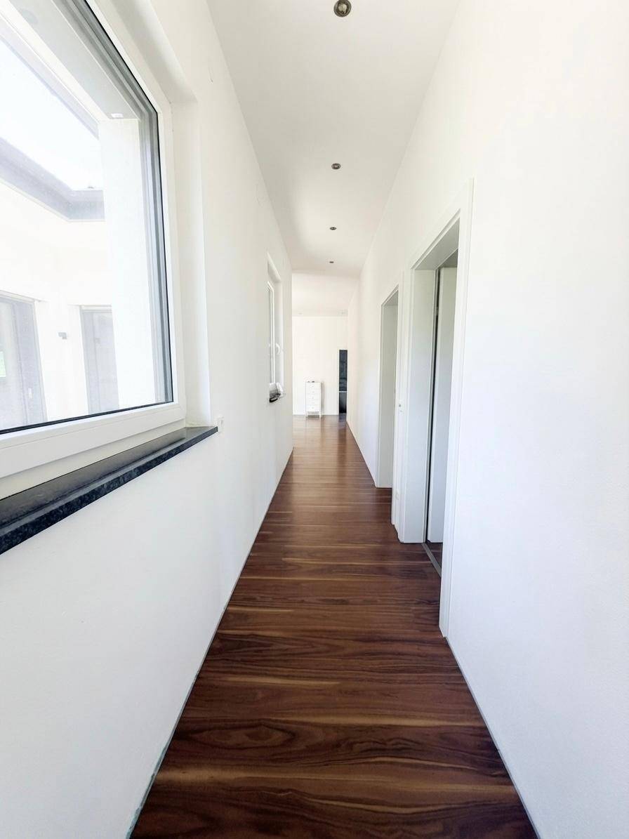 Langer, heller Flur mit dunklem Holzboden und einem Fenster, das Tageslicht hereinlässt.