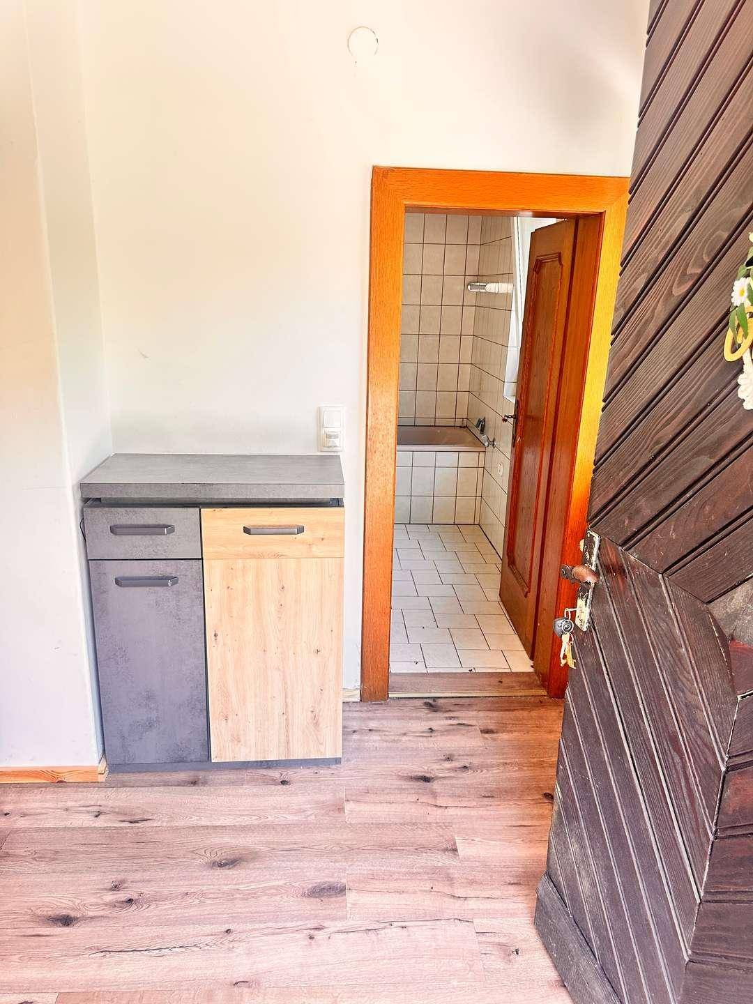 Heller Flur mit Holzoptikboden und einem kleinen Schrank, der zum Badezimmer führt.