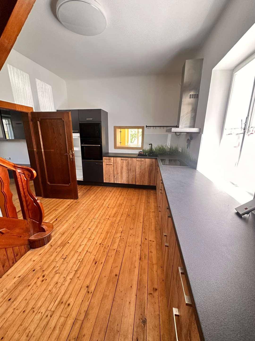 Moderne Küche mit Holzfronten, integrierten Geräten und dunkler Arbeitsplatte, hell beleuchtet.