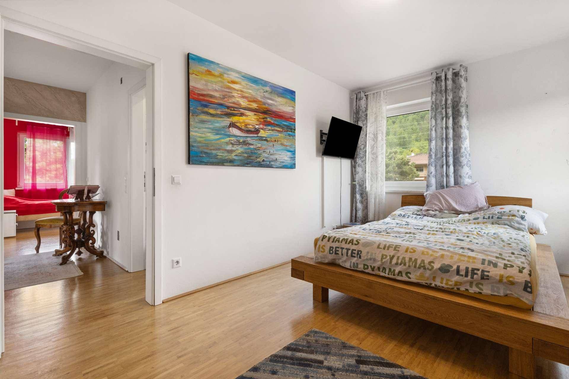 Schlafzimmer mit Holzbett, Fernseher und Zugang zu einem angrenzenden Raum.
