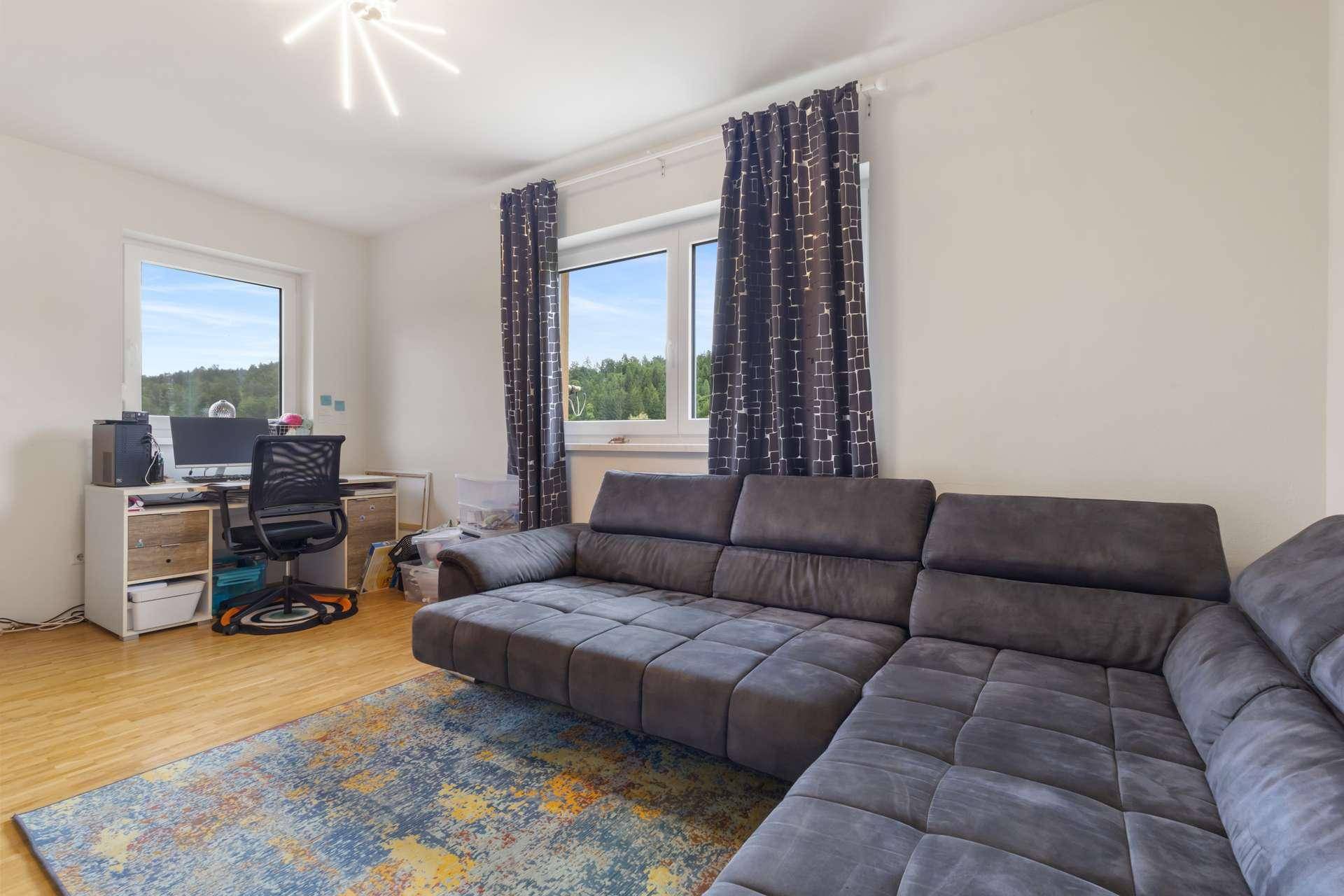 Geräumiges Wohnzimmer mit großem Sofa, Arbeitsbereich und weitem Blick ins Grüne.