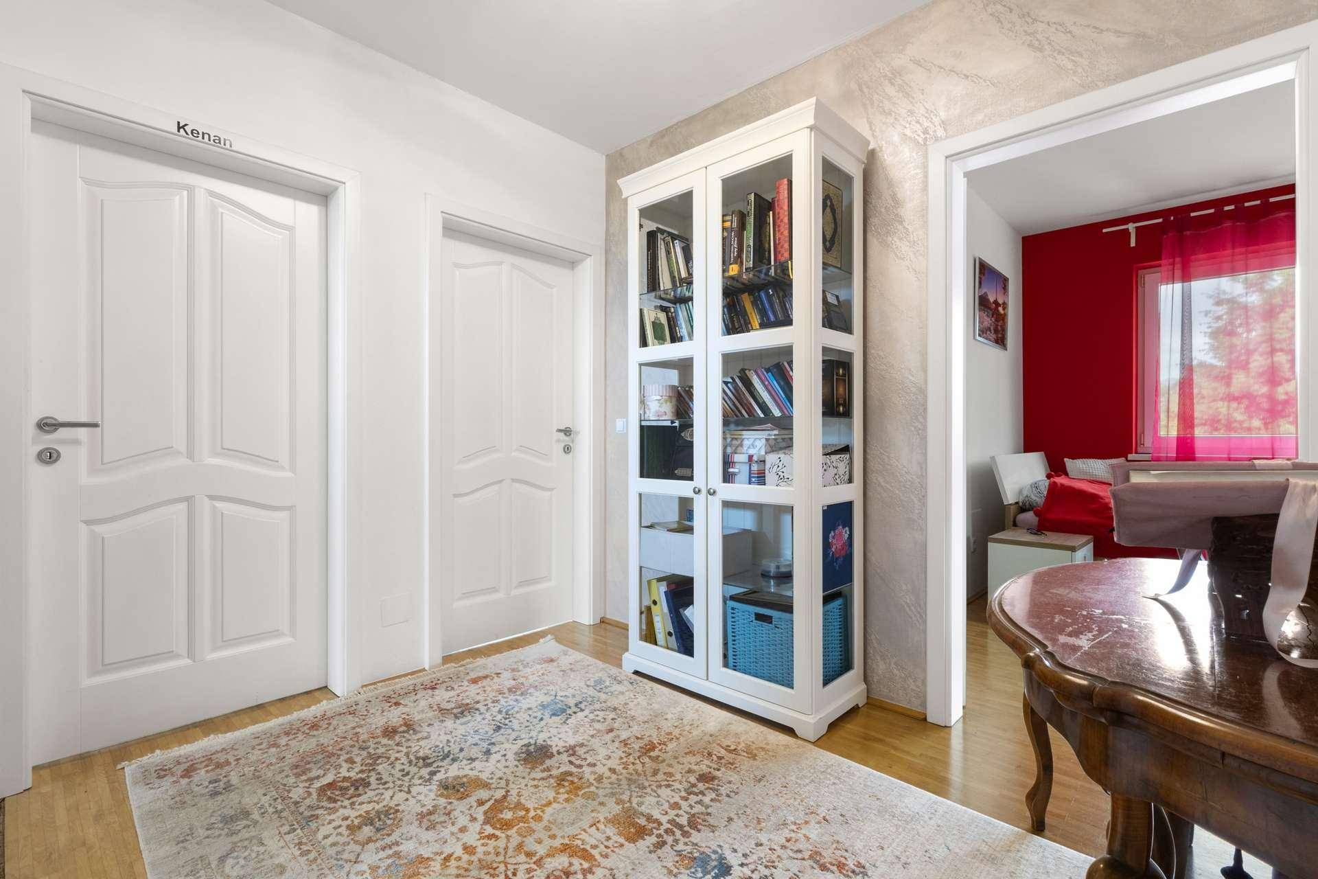 Flur mit weißem Bücherregal, Holzboden und Zugang zu weiteren Zimmern.
