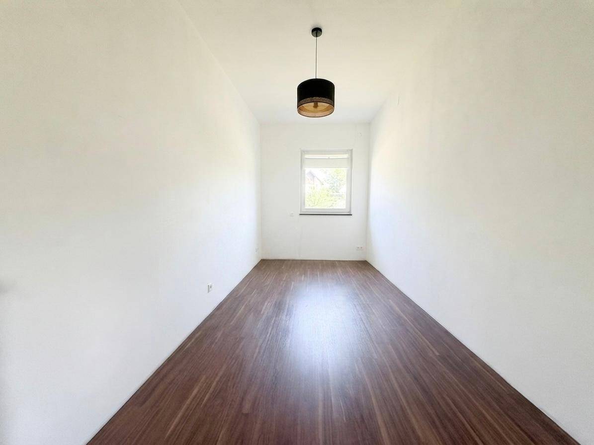 Schmaler, heller Raum mit Holzboden und einem Fenster, das für ausreichend Tageslicht sorgt.