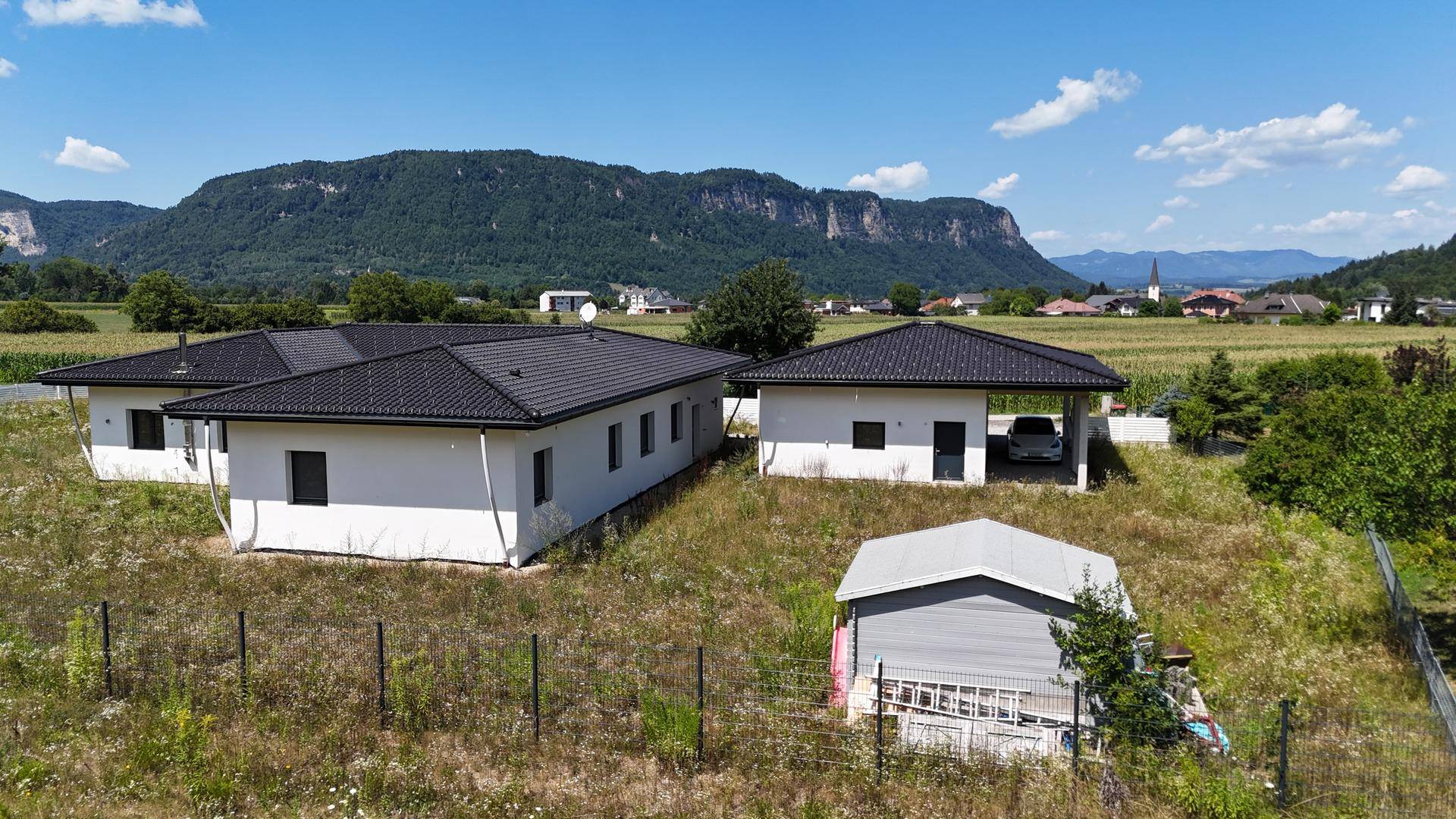 Gesamtansicht der beiden Gebäude auf dem Grundstück mit beeindruckendem Bergpanorama im Hintergrund.
