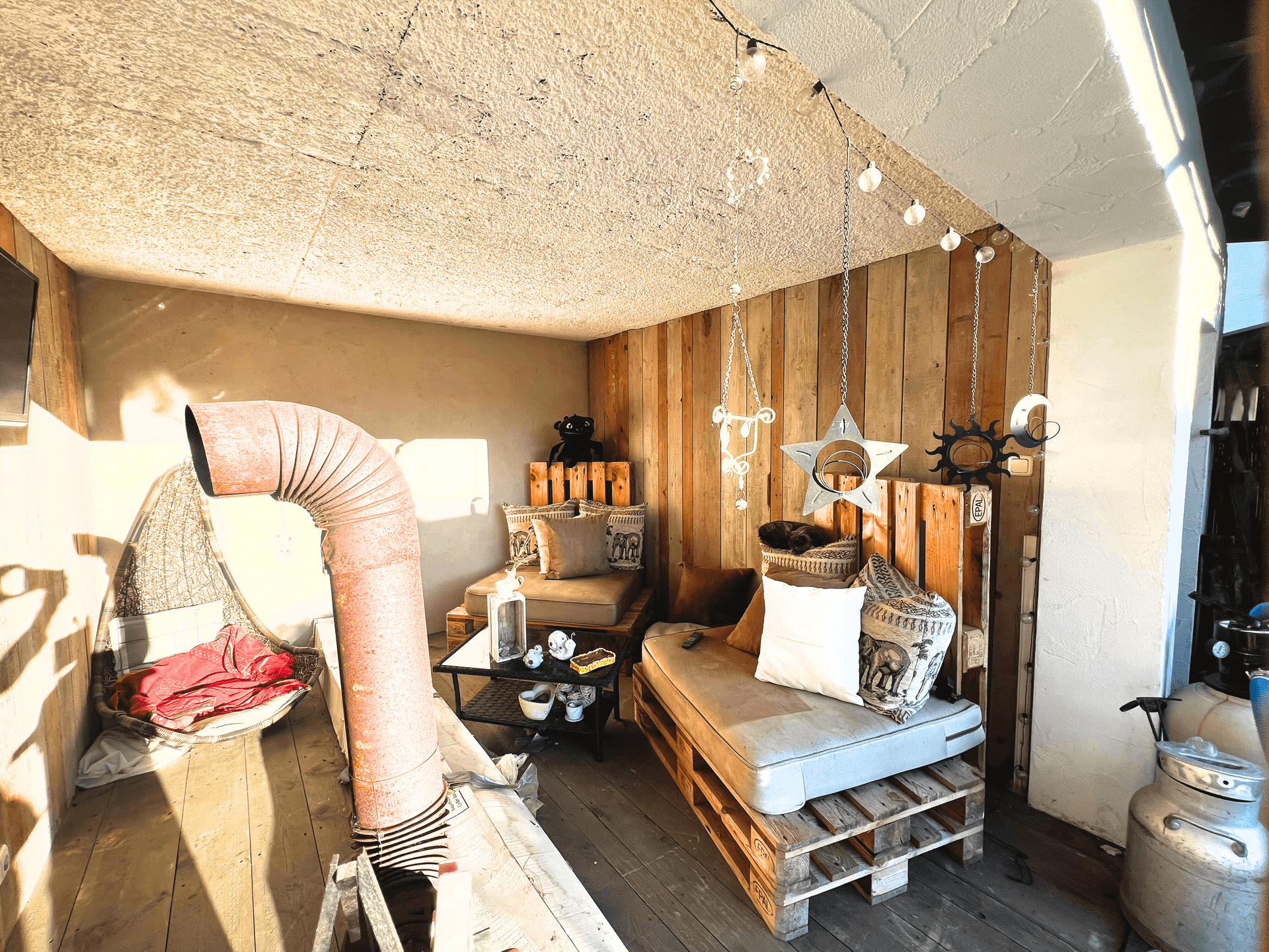 Gemütliche Loggia mit Holzwänden, Palettenmöbeln und dekorativer Beleuchtung.