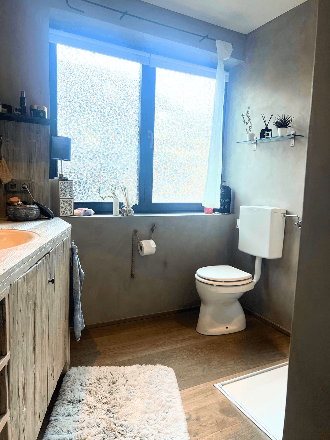Badezimmer mit Toilette, Fenster und einem Waschtisch aus hellem Holz.