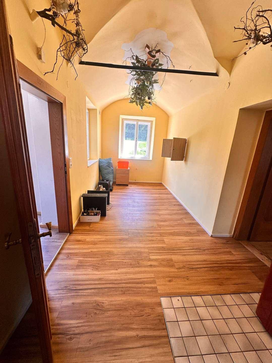 Langer Raum mit gewölbter Decke und Holzoptikboden, hell durch ein Fenster beleuchtet.