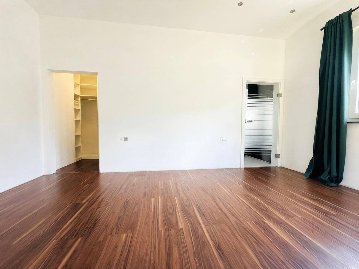 Geräumiges Schlafzimmer mit dunklem Laminatboden, Zugang zu einem begehbaren Kleiderschrank und Bad.