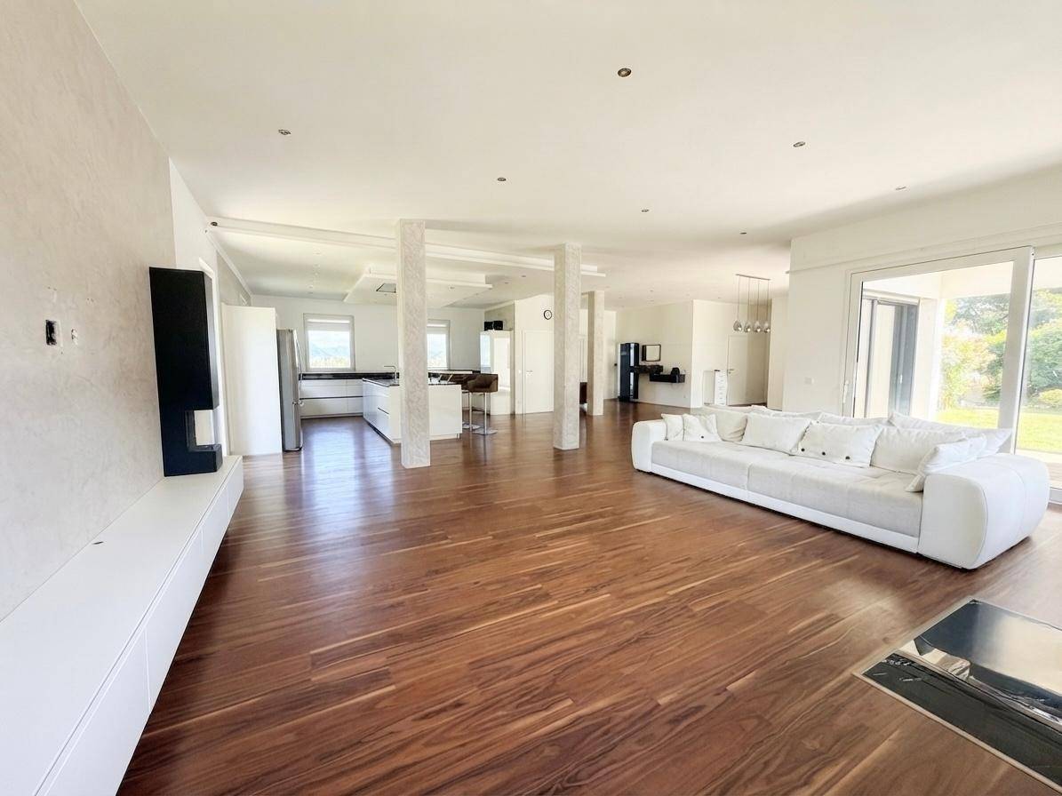 Weitläufiger offener Wohnbereich mit moderner weißer Couch, Holzboden und Blick auf die Küche.