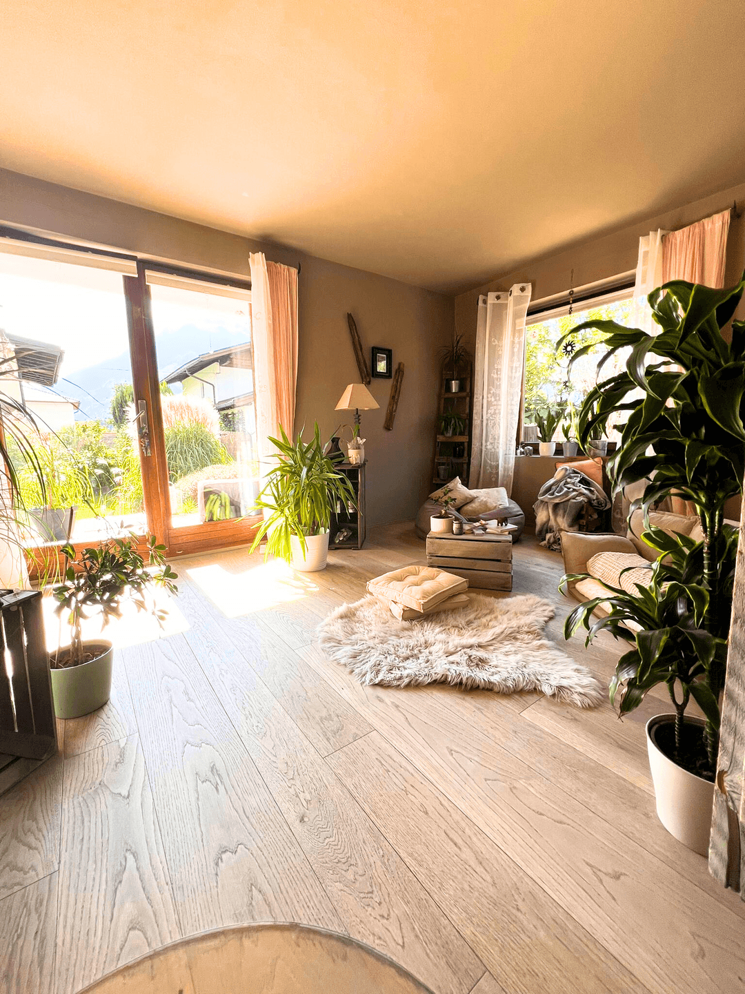 Helles Wohnzimmer mit Holzboden, großen Glastüren zum Garten und vielen Pflanzen.