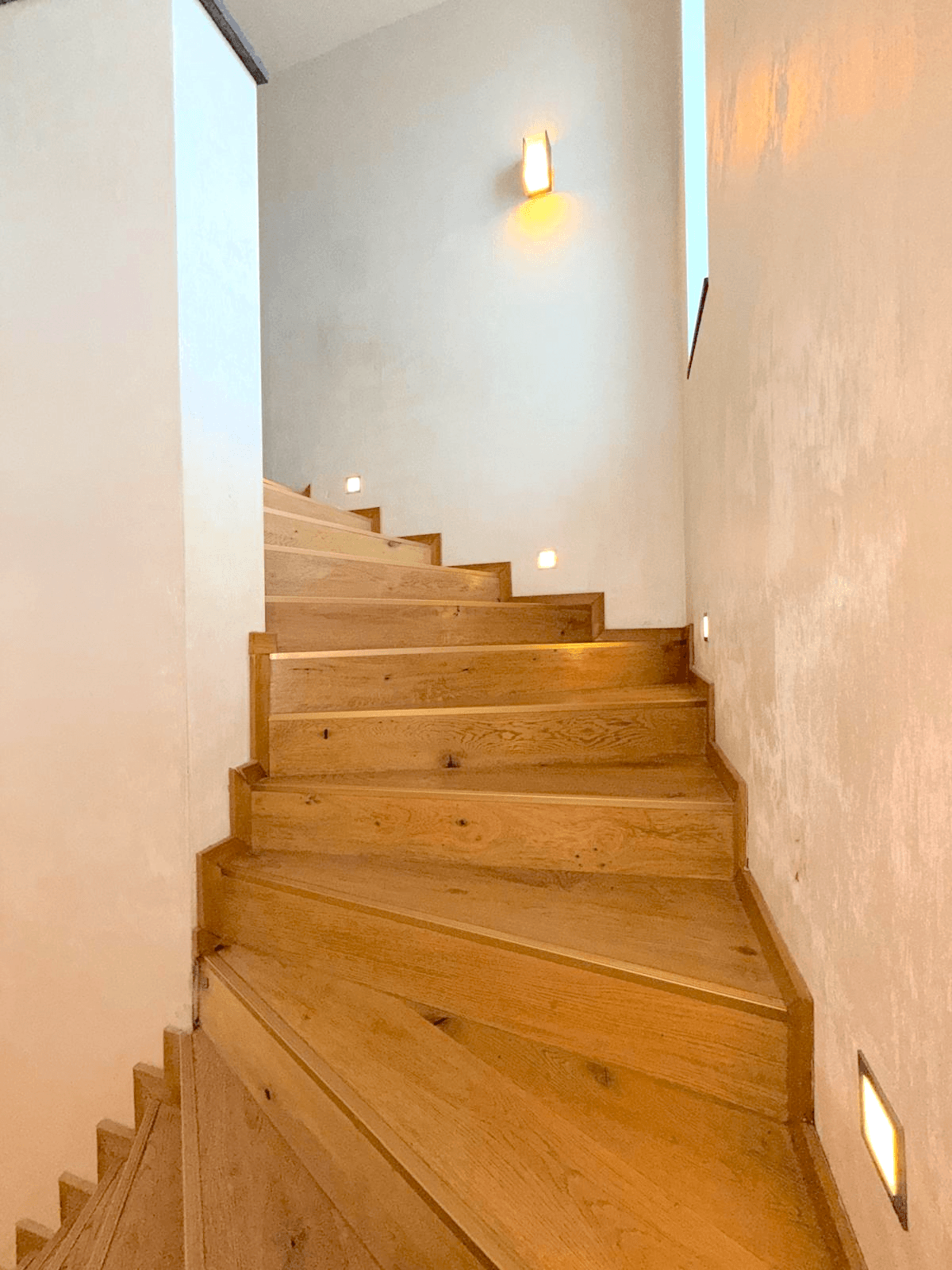 Elegante Holztreppe mit indirekter Beleuchtung, die die verschiedenen Etagen verbindet.