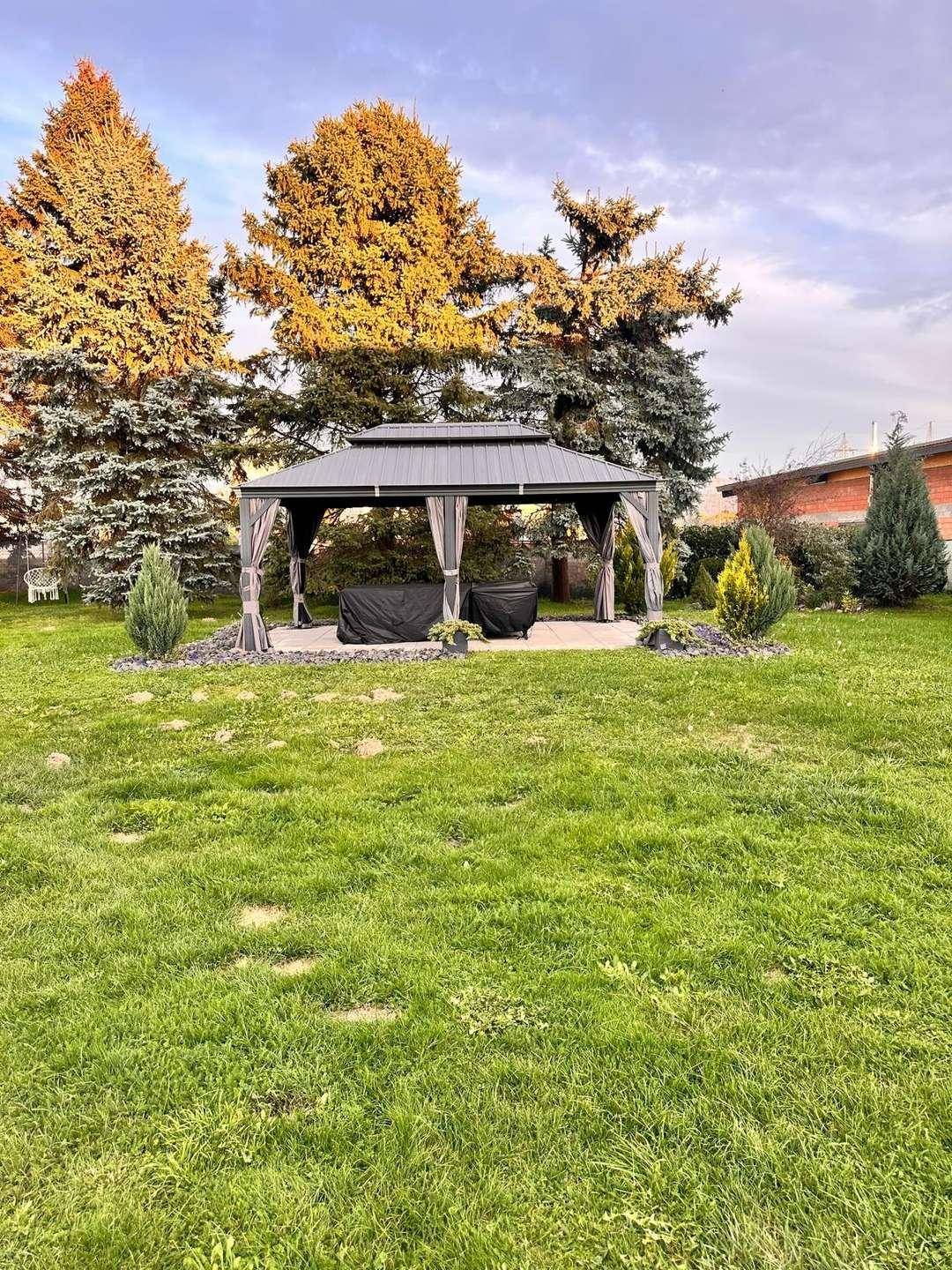 Gepflegter Garten mit großem Pavillon und hohen, alten Bäumen.