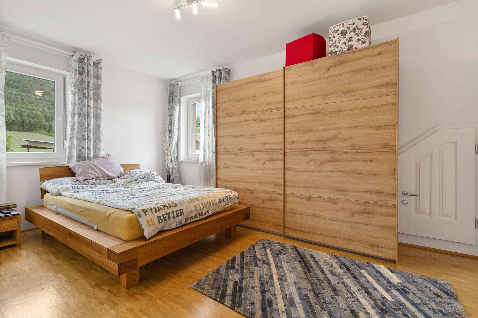 Gemütliches Schlafzimmer mit Holzbett, großem Kleiderschrank und Blick ins Grüne.