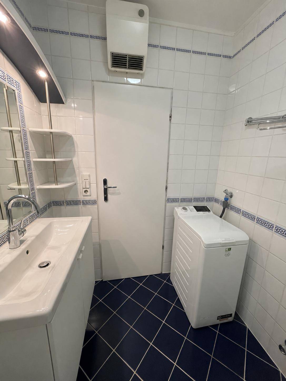 Badezimmer mit Waschmaschine, Einzelwaschbecken und weiß-blauen Fliesen.