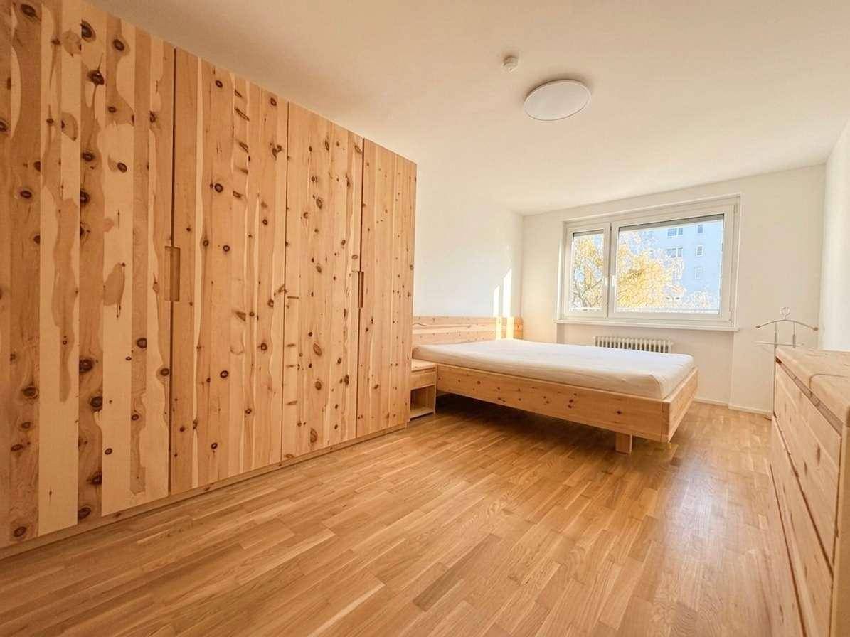 Helles Schlafzimmer mit Holzboden, großem Fenster und maßgefertigten Holzmöbeln.