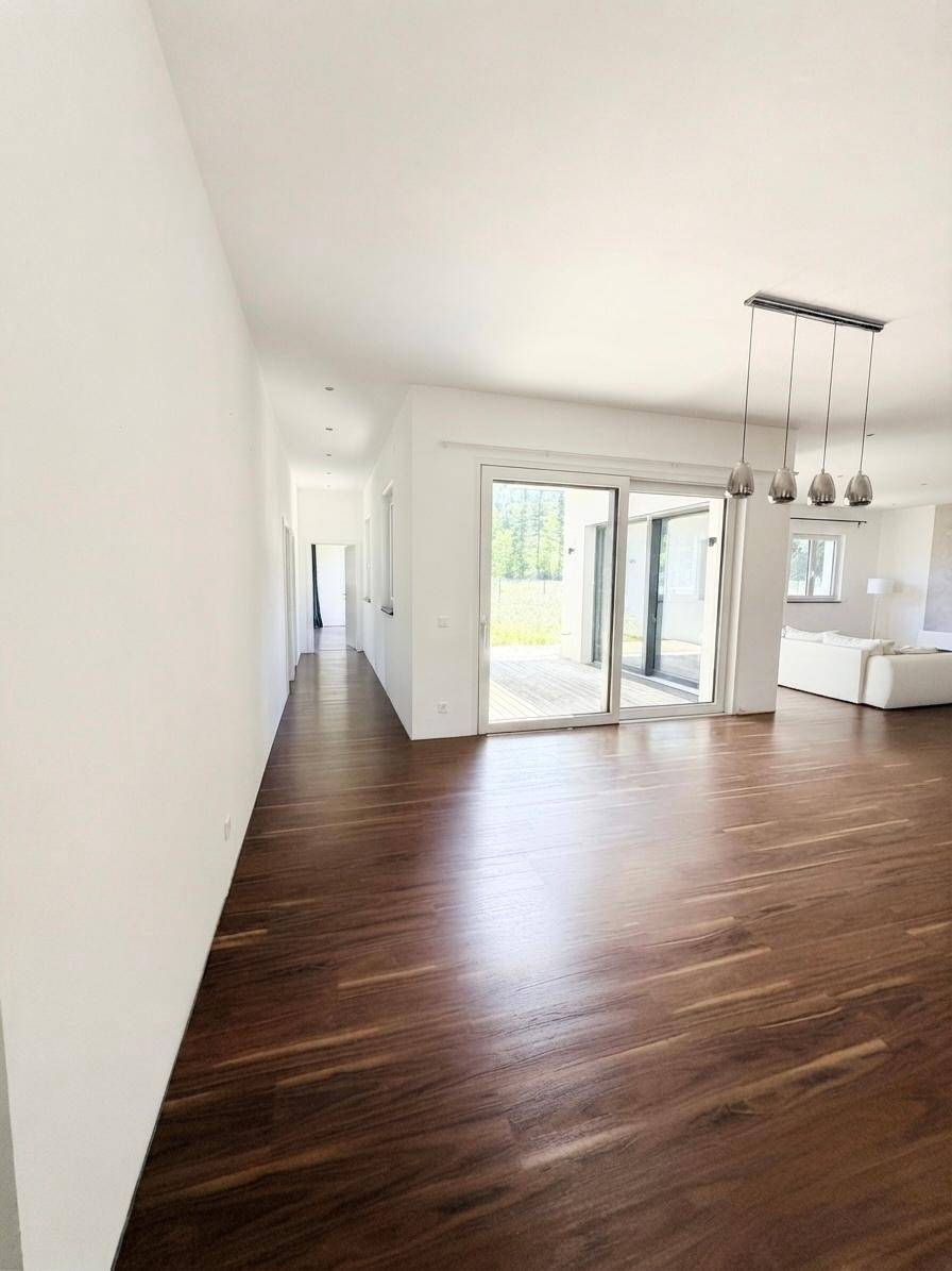 Langer, heller Flur mit dunklem Holzboden, der in den offenen Wohnbereich mit Terrassenzugang führt.