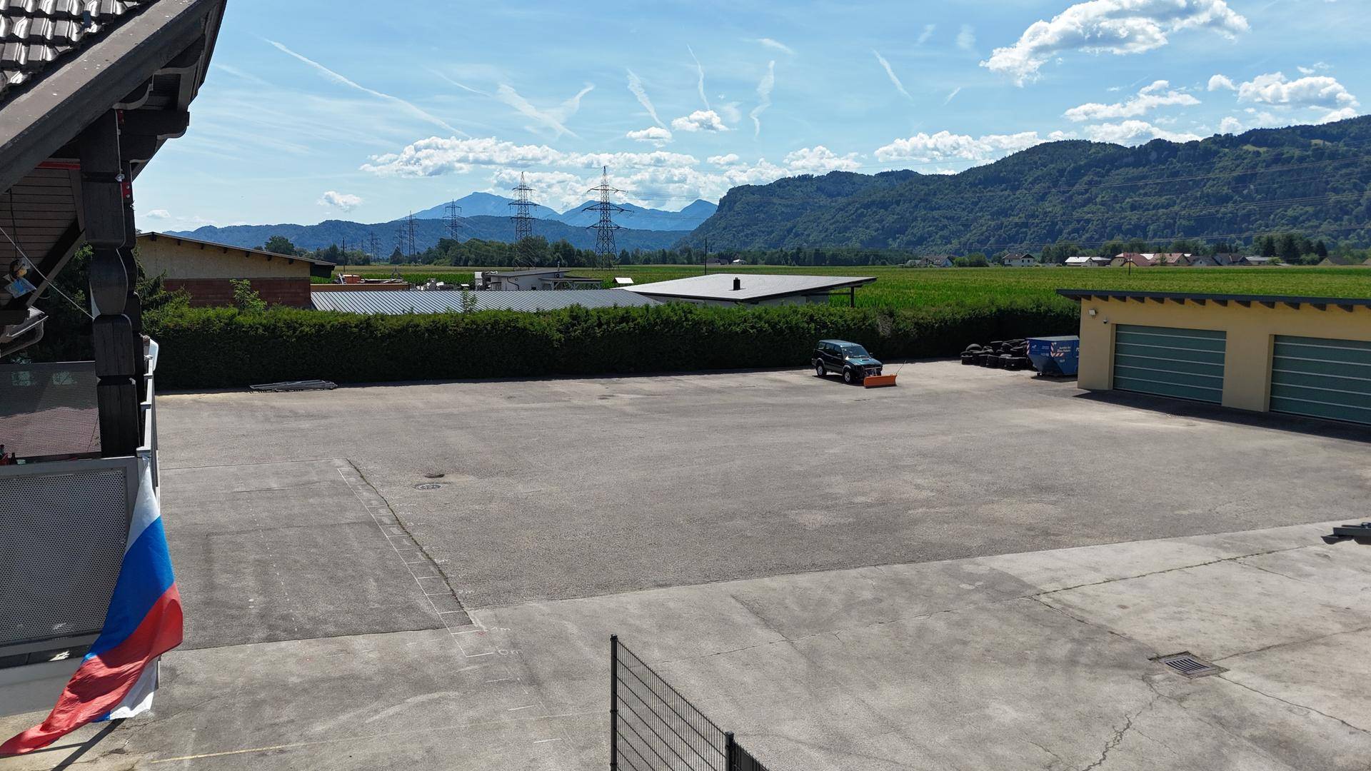 Weitläufiger asphaltierter Vorplatz eines Gewerbeobjekts mit Blick auf Felder und Berge im Hintergrund.
