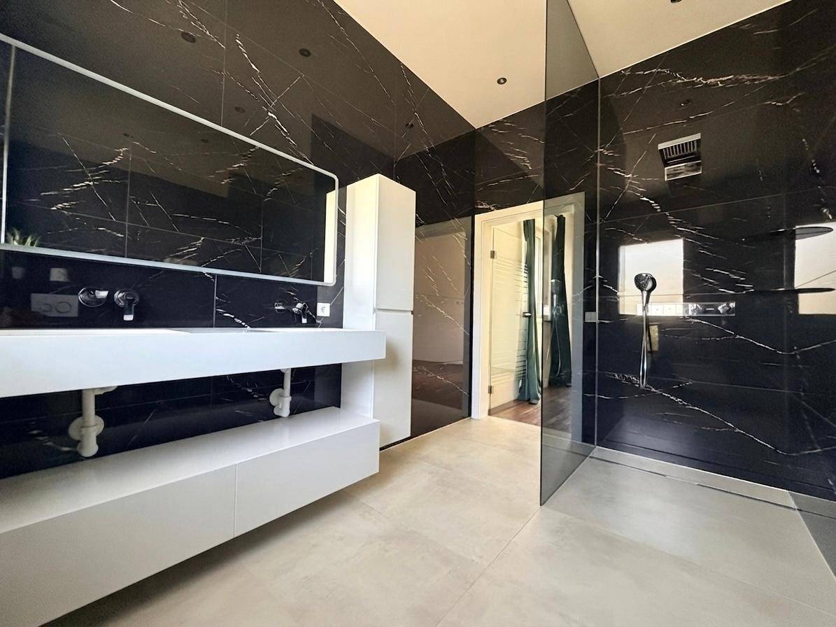 Modernes Badezimmer mit schwarzen Marmorfliesen, Doppelwaschbecken und begehbarer Dusche.
