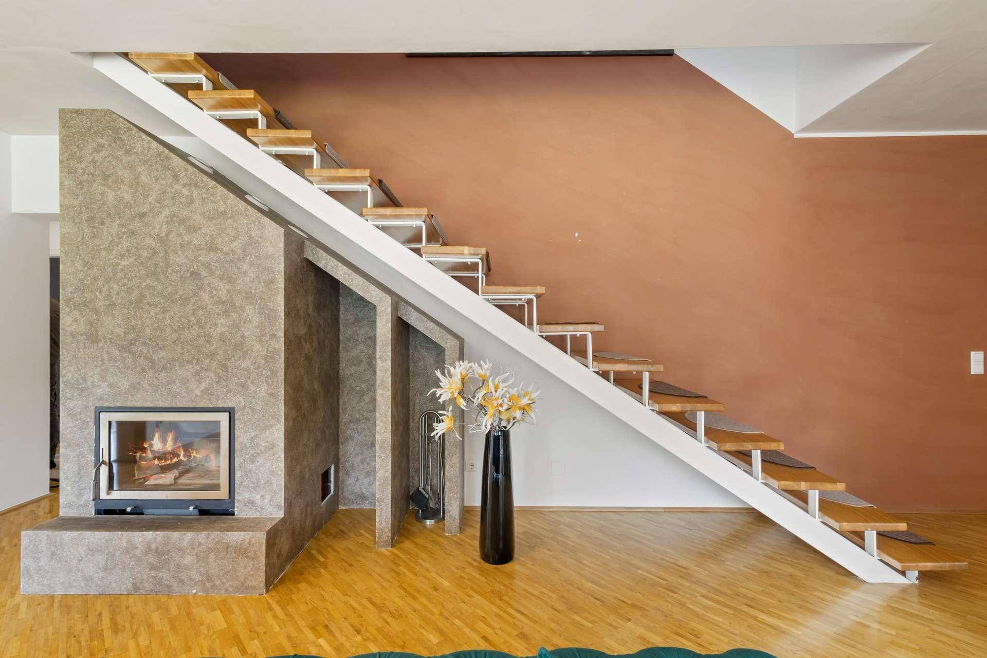 Moderner Kaminbereich im Wohnzimmer mit offener Holztreppe und Parkettboden.