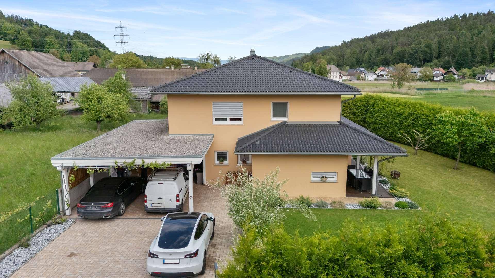 Luftaufnahme des Hauses mit gepflasterter Auffahrt, Carport und umliegendem Gartenbereich.