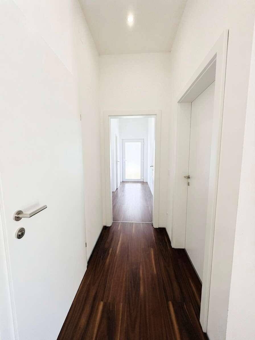 Heller Flur mit dunklem Holzboden und weißen Türen, der zu weiteren Räumen führt.