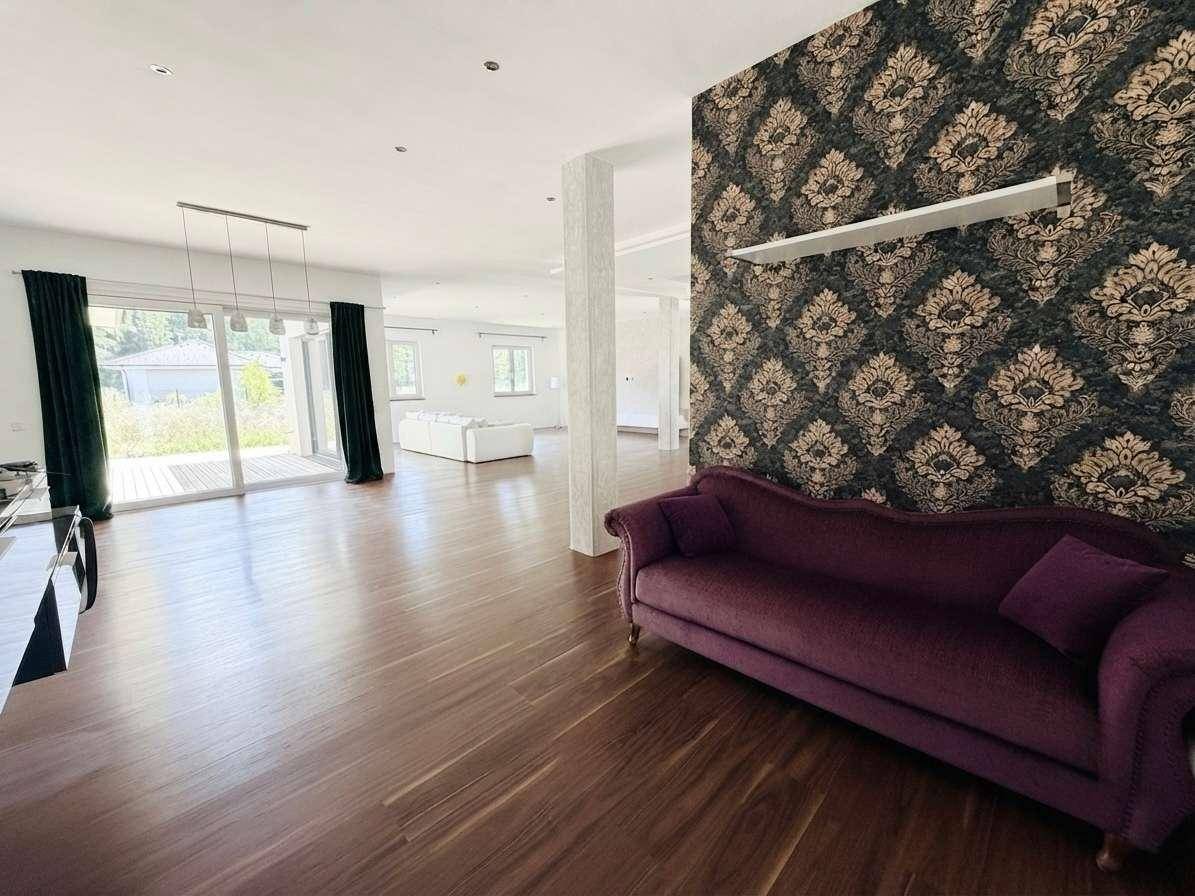 Geräumiges Wohnzimmer mit dunklem Holzboden, gemusterter Tapete und Zugang zur Terrasse.