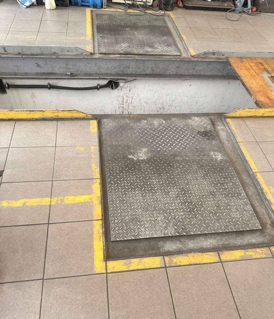 Abgedeckte Inspektionsgrube mit robusten Metallplatten in einem gefliesten Werkstattbereich.