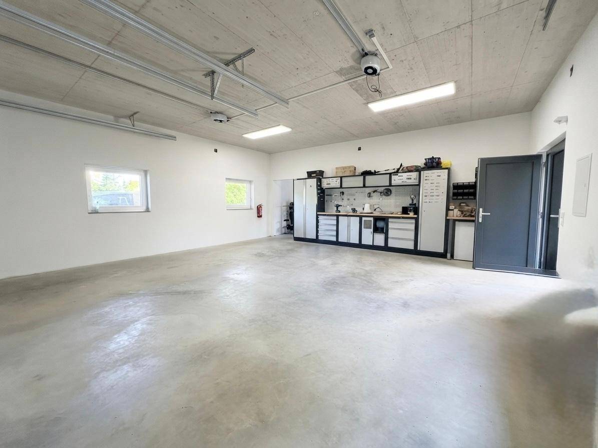 Geräumige Garage oder Werkstatt mit Betonboden, Fenstern und praktischer Werkbank.