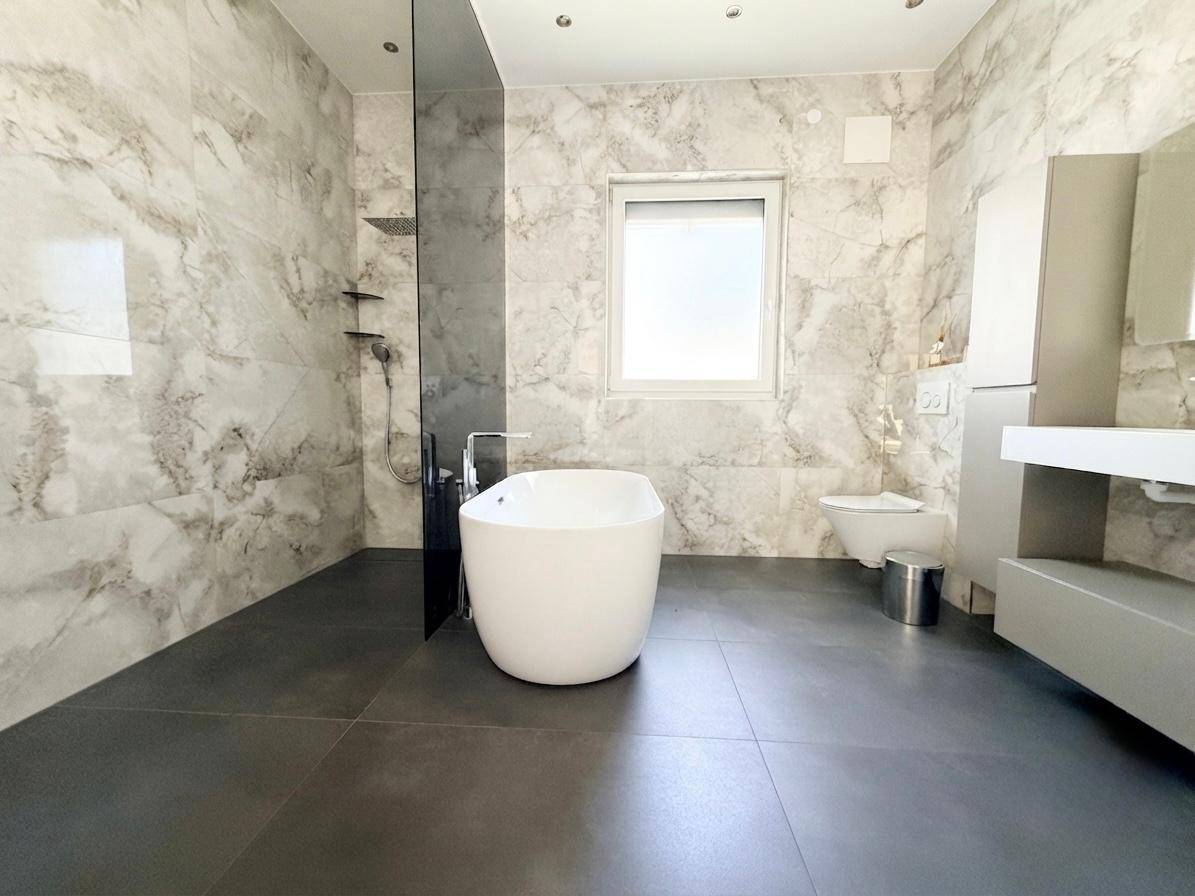 Modernes Badezimmer mit freistehender Badewanne, großer Dusche und Marmoroptik-Fliesen.