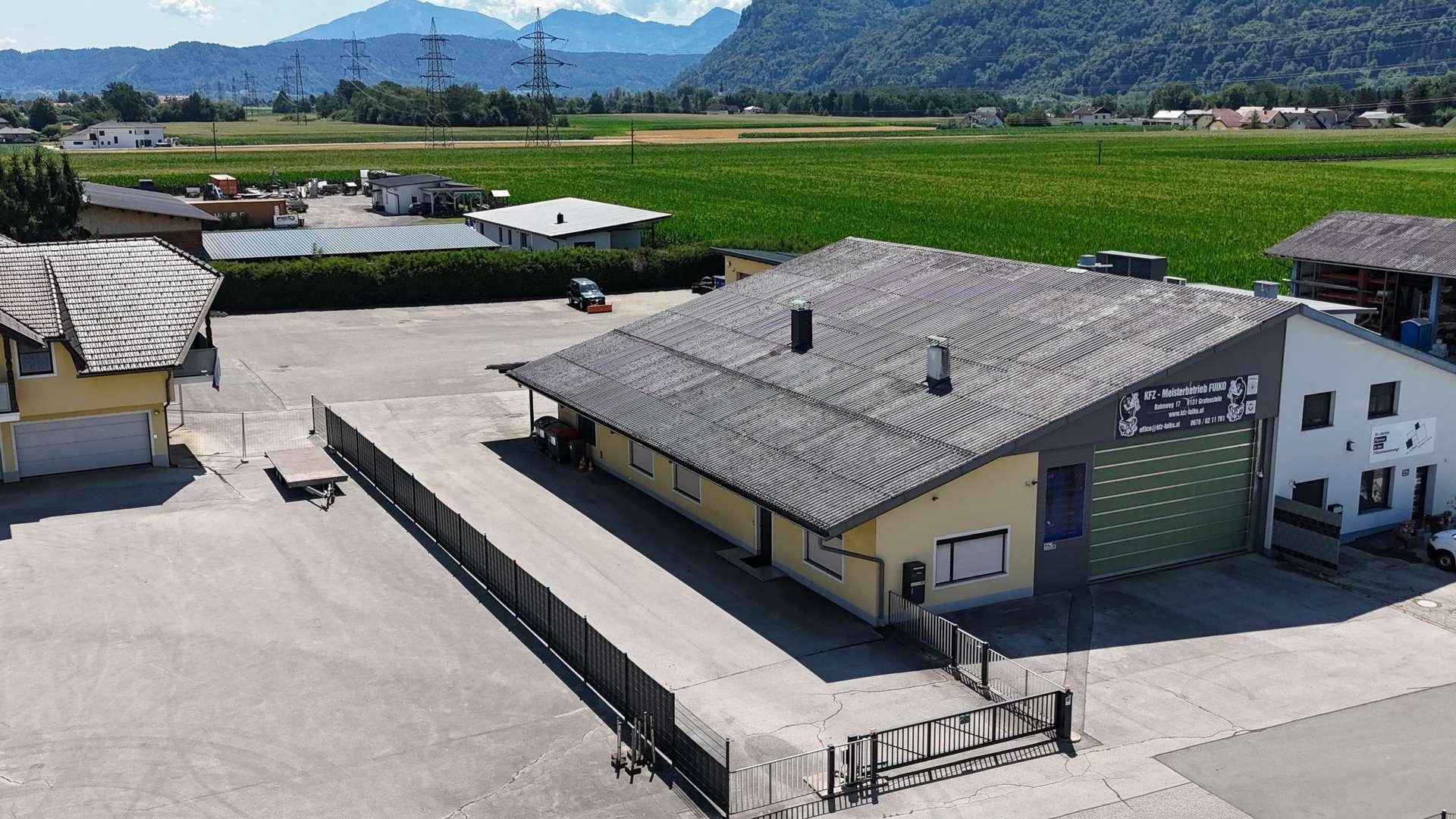 Luftaufnahme eines Gewerbegebäudes mit großer grüner Rolltor-Einfahrt und weitem Vorplatz.