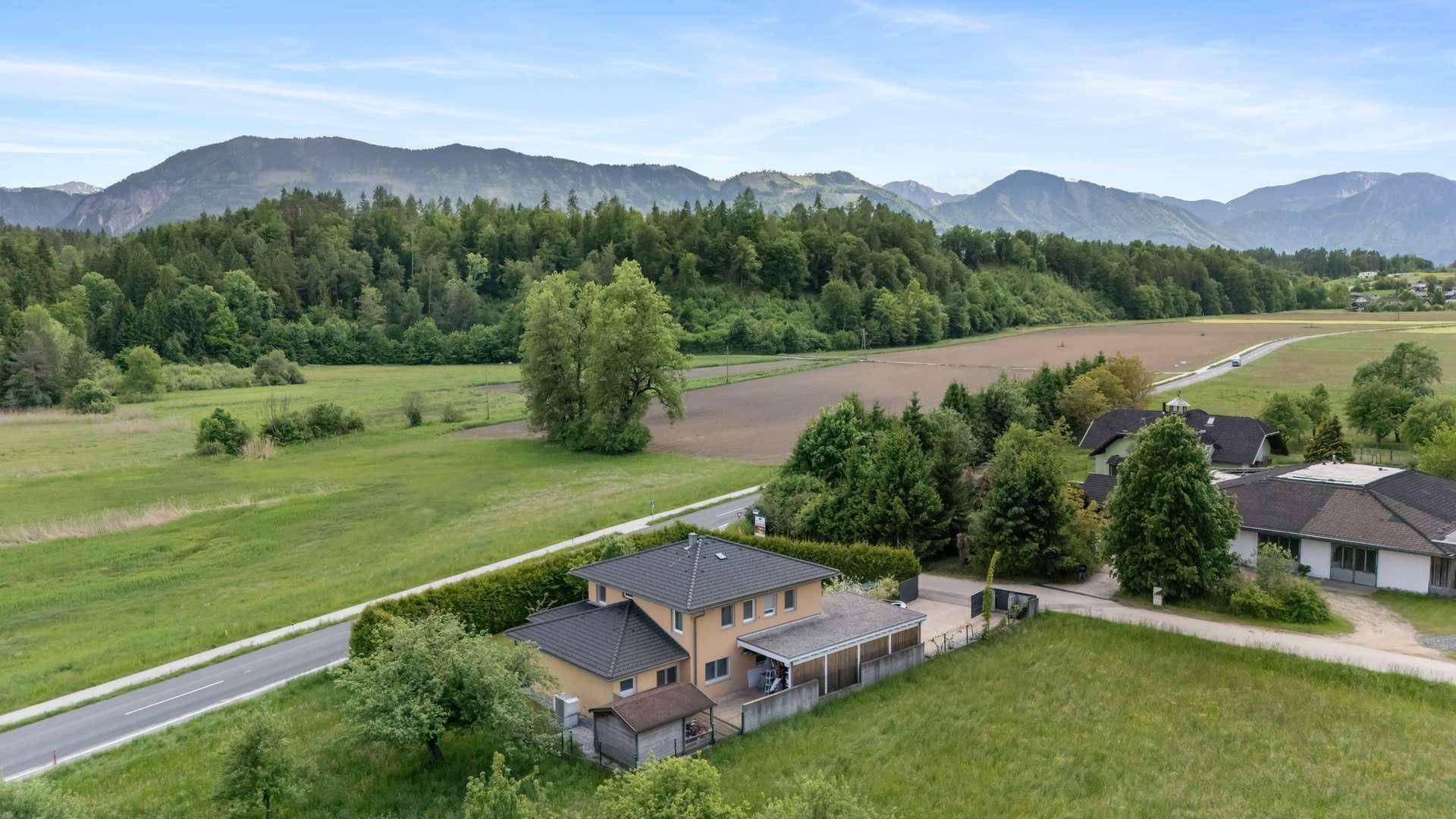 Weitläufige Luftaufnahme eines Hauses in ländlicher Umgebung mit Bergen im Hintergrund.