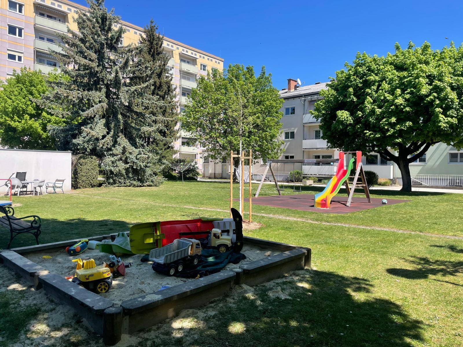 Großer Spielplatz mit Sandkasten, Rutsche und viel Grünfläche für Kinder.