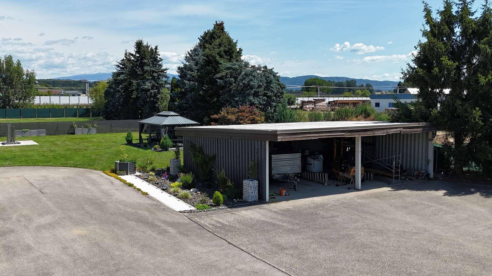 Gepflegter Gartenbereich mit Pavillon und einem Carport, angrenzend an eine asphaltierte Fläche.