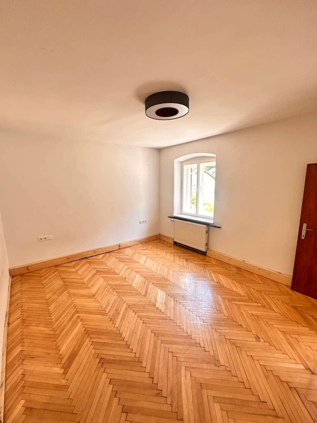 Helles Zimmer mit Fischgrätparkett, weißen Wänden und einem Fenster, sorgt für viel Tageslicht.