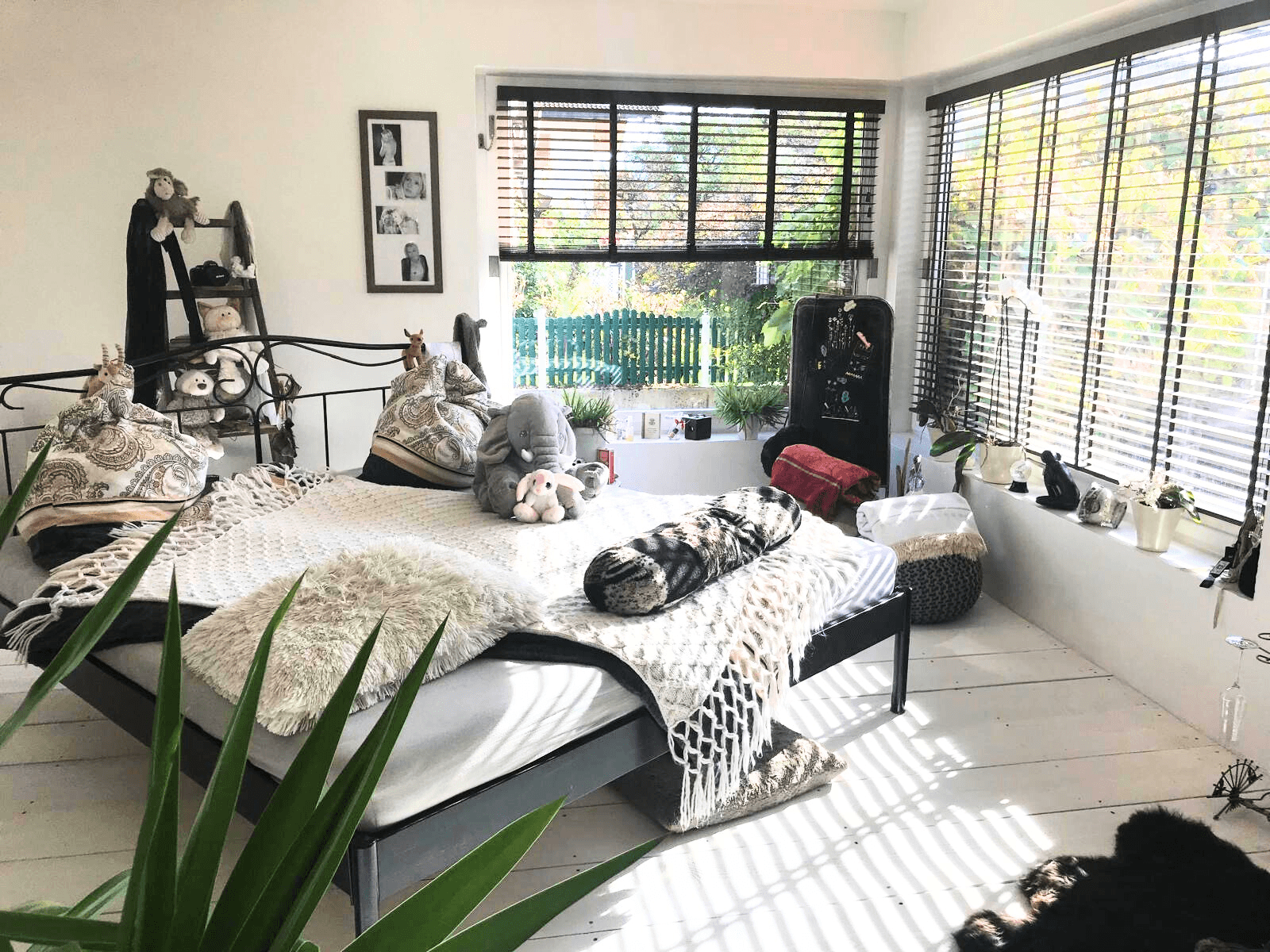 Helles Schlafzimmer mit weißem Holzboden, großem Bett und Fenstern mit Jalousien.