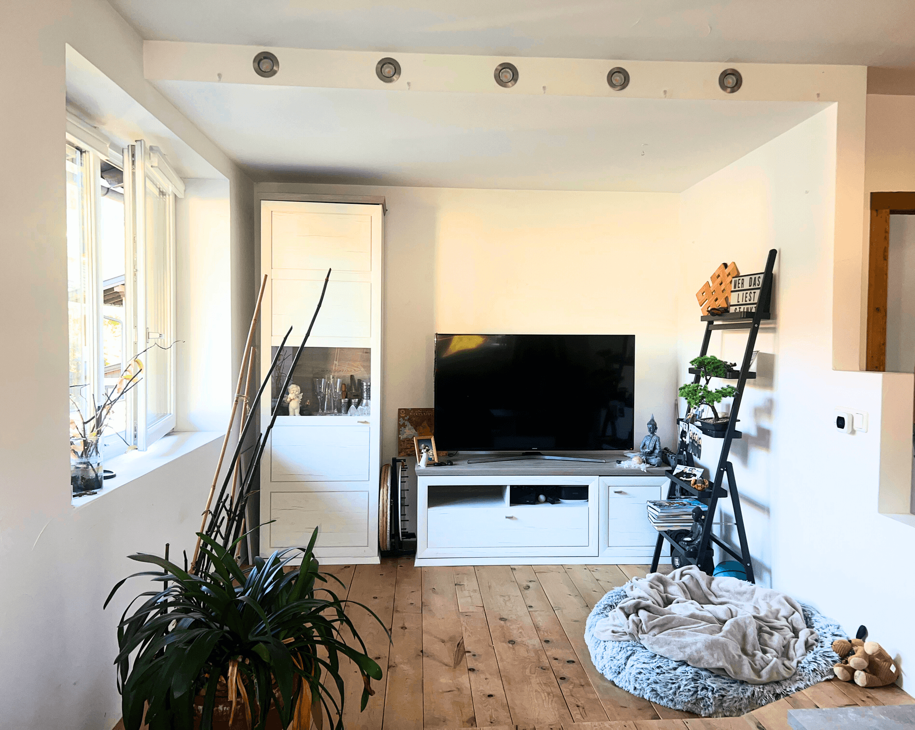 Wohnzimmer mit Fernseher, Medienschrank, weißem Vitrinenschrank und Holzboden.