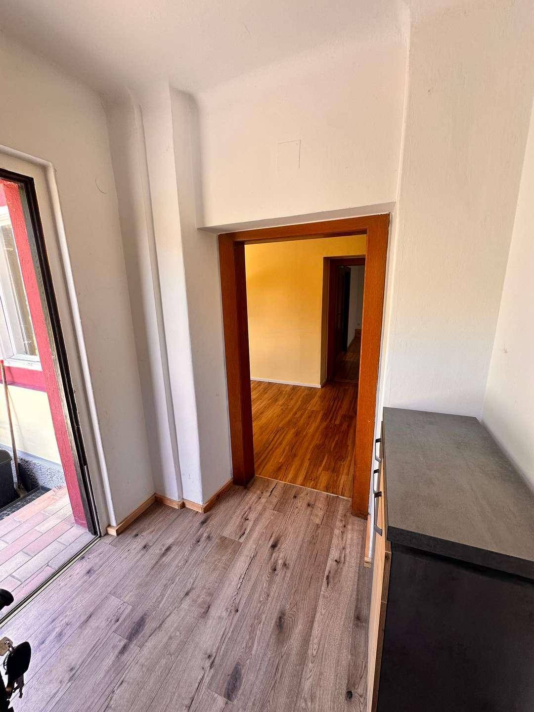 Eingangsbereich mit Holzoptikboden und Blick nach draußen, der in weitere Räume führt.