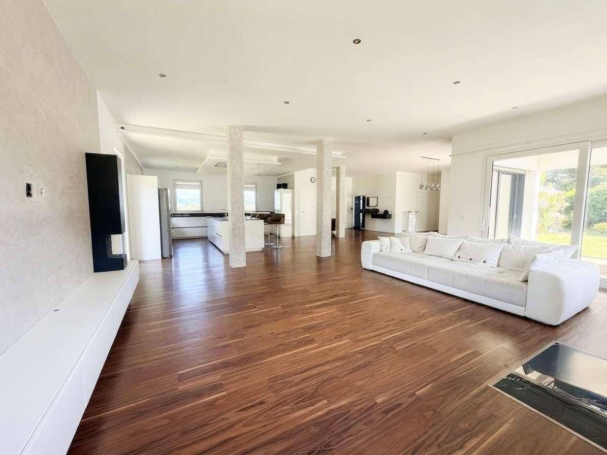 Weitläufiger offener Wohnbereich mit Holzboden, weißem Sofa und Blick auf die moderne Küche.