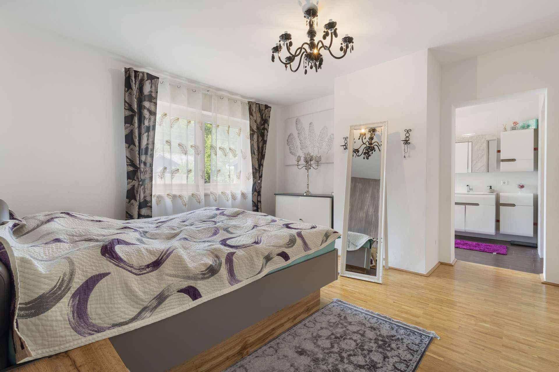 Schlafzimmer mit Doppelbett, Parkettboden und direktem Zugang zum Badezimmer.